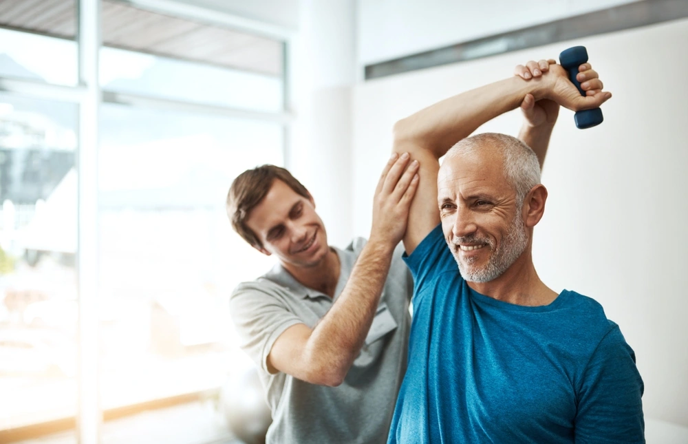 Ein mittelalter Mann wird von einer anderen Person bei der Rehabilitation betreut.