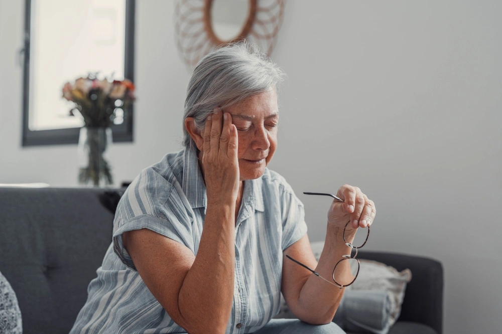Eine ältere Frau fasst sich mit schwerzverzerrtem Gesicht an den Kopf.