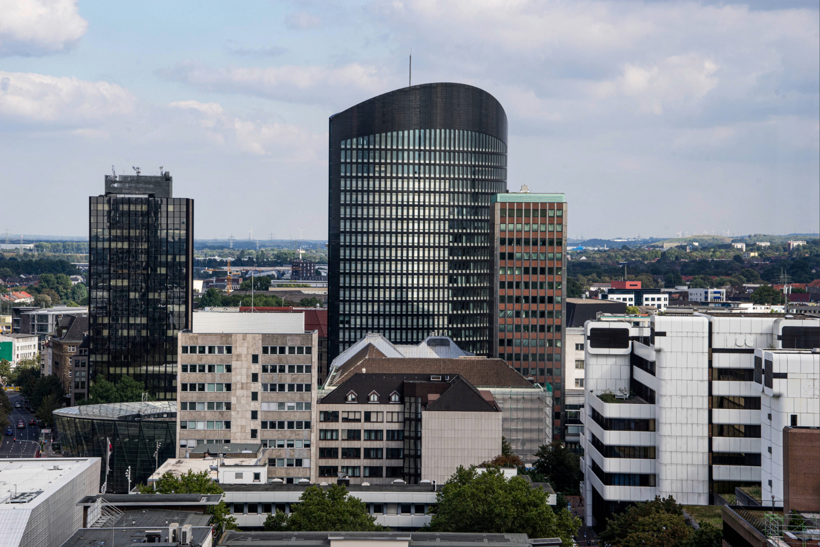 Blick auf die Dortmunder Innenstadt mit mehreren Hochhäusern, darunter ein markantes schwarzes Gebäude mit abgerundeter Fassade, vor bewölktem Himmel.